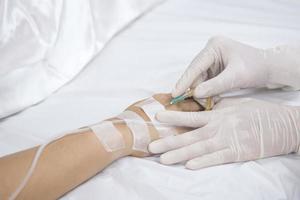 cerrar la mano del médico inyecta una aguja de infusión salina en el paciente en la cama foto