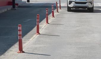 Row of orange plastic traffic poles with blurred motion front view of white car slow driving into outdoor parking lot area photo