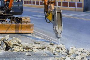 el enfoque selectivo del martillo triturador hidráulico de la excavadora está rompiendo el pavimento en el área de la carretera para prepararse para instalar el proyecto del sistema de alcantarillado foto