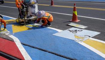 Road workers group with thermoplastic spray road marking machine are working to paint traffic sign and bicycle lane on asphalt road with railway track crossing on street surface photo