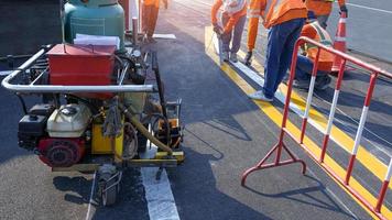 Road workers group with thermoplastic spray road marking machine are working to paint traffic lines on asphalt road with railway track crossing on street surface