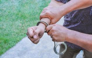 Close up plainclothes police man's hand handcuffing young villain man with blurred outdoor background photo