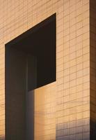 Morning sunshine on surface of geometric apertures window on gray tile wall of modern office building in perspective side view