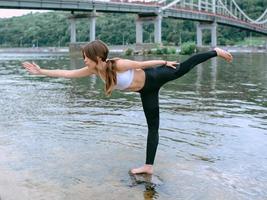 young fit woman in sportswear in different yoga asanas outdoor on the beach by the river. Yoga, nature, city and sport concept photo