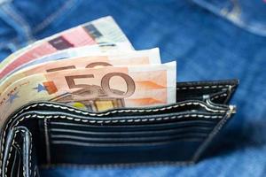 dinero en euros, billete en euros dentro de una cartera de cuero negro sobre fondo de jean. foto