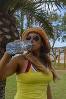 mujer feliz bebiendo agua mineral junto a una palmera disfrutando del verano. espacio de copia. foto