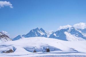 Tracks on snow covered landscape slope against blue sky photo