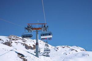 Cable cars traveling over snow covered mountain slope against clear blue sky photo