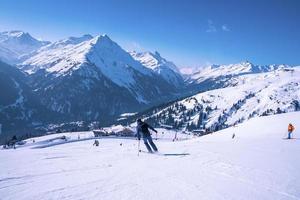 Skiers skiing on slope against snowy mountain range