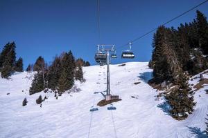 Ski lift passing amidst trees over snowy mountains