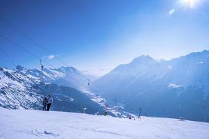 Skiers at t-bar ski lift on snowy hill slope against sky photo