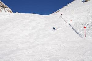 Distant skier sin sportswear skiing on snowy mountain against sky photo