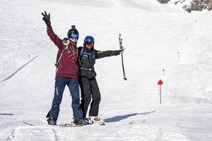 Snowboarder and skier with arms outstretched standing on mountain slope photo