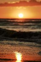 reflejo de la luz del atardecer en la superficie de la arena del mar, hermosa luz del sol amarilla en la espuma del mar, playa de arena cálida foto