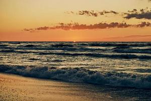 Beautiful sunset over sea waves, half sun below horizon, seacoast view, amazing seascape photo