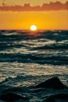 Yellow sun almost down horizon over deep blue sea, atmospheric view from rocky sea beach photo