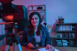 hermosa mujer hispana frente a una cámara de video grabando un blog en su estudio con luces rojas y azules dentro de su casa