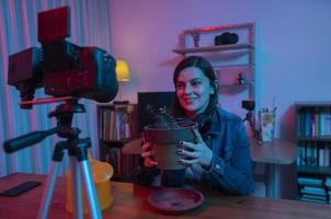 hermosa mujer hispana frente a una cámara de video grabando un blog en su estudio con luces rojas y azules dentro de su casa foto