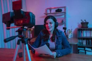 hermosa mujer hispana frente a una cámara de video grabando un blog en su estudio con luces rojas y azules dentro de su casa foto