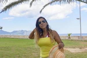 retrato de una mujer latina sonriendo, divirtiéndose, de vacaciones en mallorca posando en un cálido día de verano de primavera, bajo una palmera, concepto de vacaciones foto