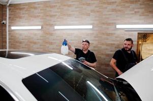 Worker in detailing garage put polyurethane anti-gravel film cover in white luxury car. photo