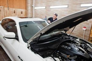 Worker in detailing garage put polyurethane anti-gravel film cover in white luxury car. photo