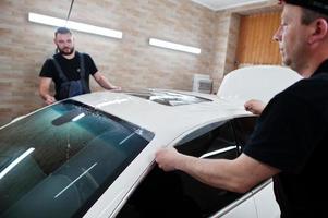 Worker in detailing garage put polyurethane anti-gravel film cover in white luxury car. photo