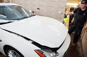 el trabajador en el garaje de detalles puso una cubierta de película antigravilla de poliuretano en un automóvil de lujo blanco. foto