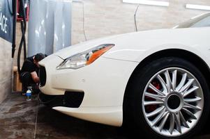 Worker in detailing garage put polyurethane anti-gravel film cover in white luxury car. photo