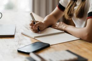 Close up of student girl hand writing on notebook on a desk at home. photo