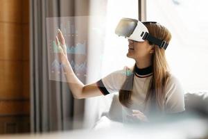 imagen conceptual de una mujer de negocios segura y exitosa en traje sentada dentro de un edificio de oficinas con interfaz financiera y usando auriculares de realidad virtual. foto