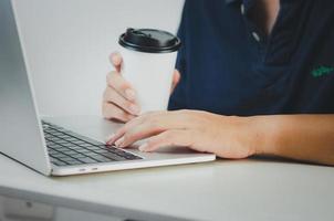 man using computer laptop and coffee cup paper searching internet, sending sms, using text messenger or online banking on desk. photo
