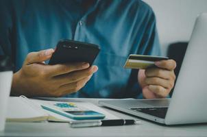 mano de hombre con tarjeta de crédito y teléfono móvil compras en línea comercio electrónico y banca por Internet en el escritorio. foto