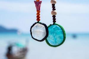 Close-up colorful handmade keychains made of crystal stones with blue sea background. Popular as a gift or souvenir.