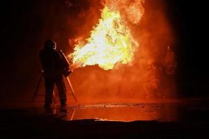 los bomberos usan ropa de protección contra incendios para rociar fuego de los tanques para simulacros de incendio nocturnos.