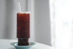 Iced black coffee or americano in tall glasses with straws and coasters on a window table in a minimalist cafe. Copy space.