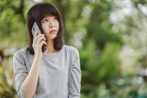 Woman talking on the phone and and looking sideways with blurred nature background. Copy space. photo