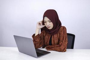 Young Asian Islam woman is serious look with thinking gesture hand on face on the front of Laptop. photo