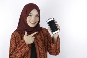 Young Asian Islam woman is smiling pointing on smartphone standing on white background. photo