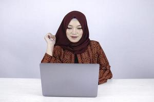 Young Asian Islam woman is smiling face with thinking gesture looking on the blank space in the front of laptop photo