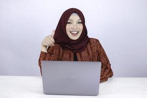 Young Asian Islam woman is smile and happy when working on a laptop with ok hand sign. photo