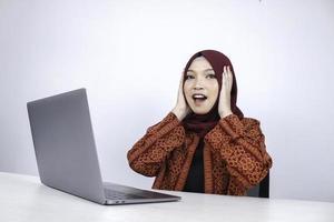 Young Asian Islam woman wearing headscarf is shocked and excited with what she see on laptop on the table. photo