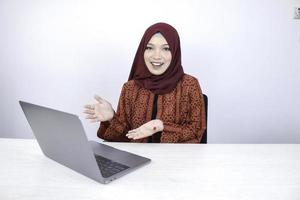 una joven islámica asiática sonríe señalando con la mano cuando trabaja en una laptop con fondo blanco. foto