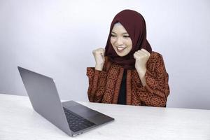 Young Asian Islam woman wearing headscarf is shocked and excited with what she see on laptop on the table. photo