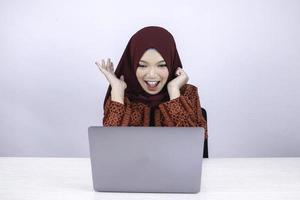 Young Asian Islam woman wearing headscarf is shocked and excited with what she see on laptop on the table. photo