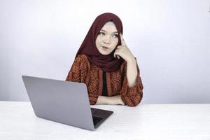 Young Asian Islam woman is serious look with thinking gesture hand on face on the front of Laptop. photo