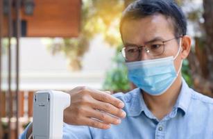 hombre revisando la fiebre con termómetro digital para escanear y proteger del coronavirus en la cafetería, conceptos de atención médica foto