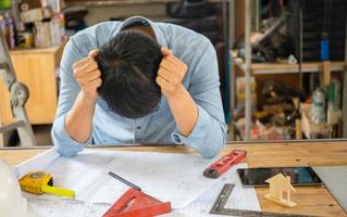 un joven ingeniero serio sentado en la mesa planificando el trabajo en la habitación, un hombre con dolor de cabeza en un taller