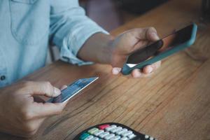 hombre con tarjeta de crédito y teléfono inteligente con máquina de pago en la mesa en la cafetería, conceptos de pago en línea