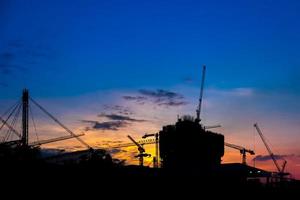 grúas de construcción industrial y siluetas de edificios durante la puesta de sol foto